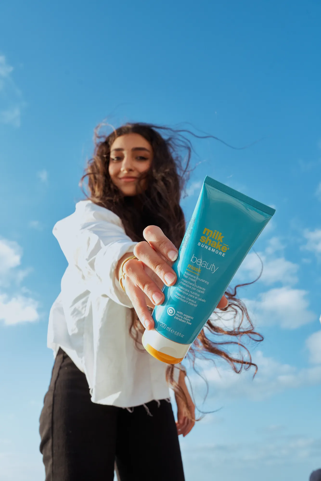 A woman holding a blue Capello tube toward the camera against the sky