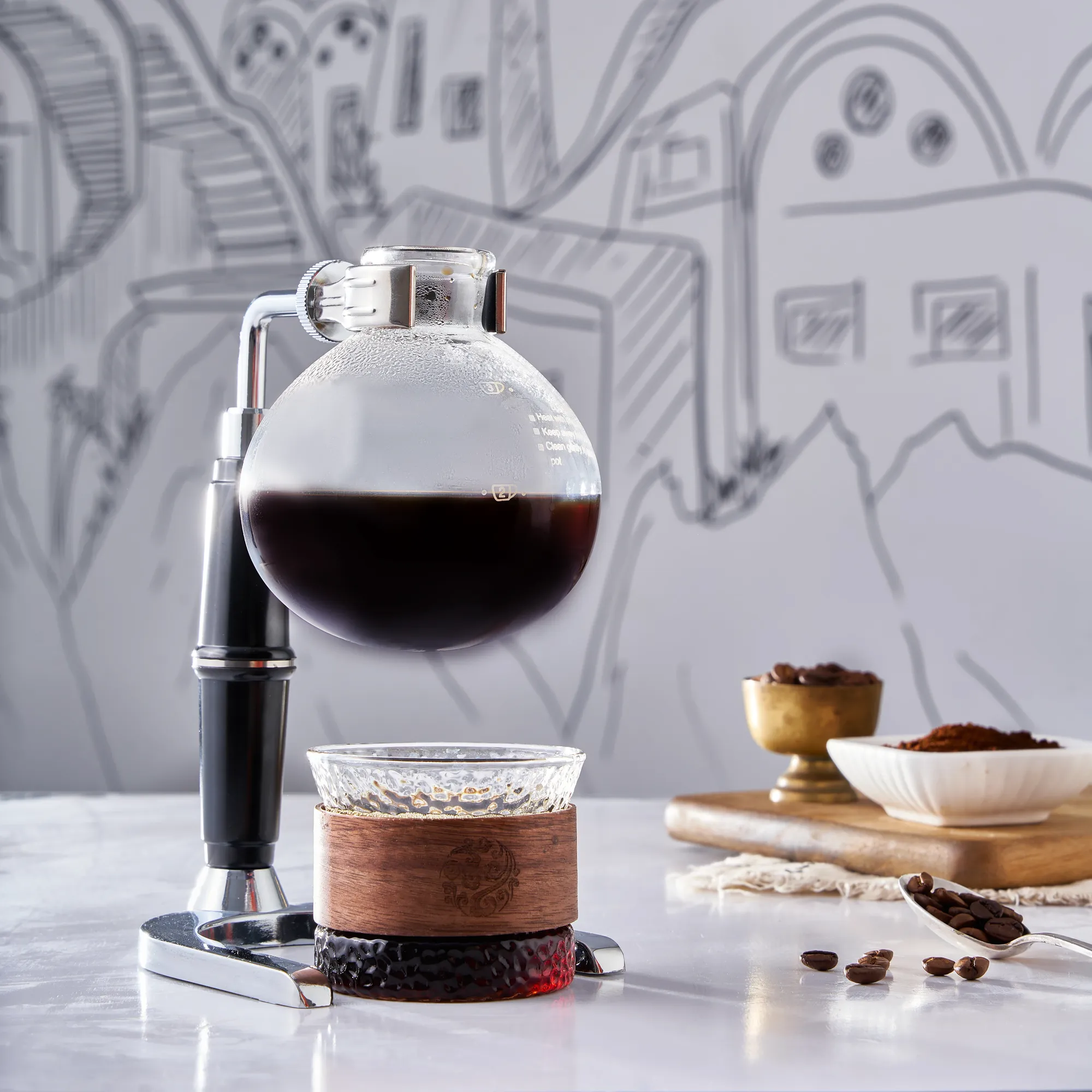 A syphon coffee brewer in front of a hand-drawn wall